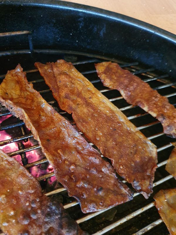 Leg de stroken op het bbq rooster, indirect! Begin zover mogelijk van de hitte vandaan. Gedurende het draaien zullen ze droger en minder slap worden.
Als laatste leg je ze direct boven de kolen. Goed in de gaten houden dat ze niet verbranden. Door ze boven de kooltjes te leggen gaan ze eruit zien als uitgebakken bacon